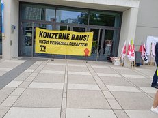Ein gelbes Banner hängt an einer Glasfront an einem großen Gebäude.