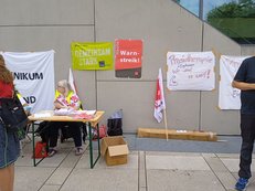 Mehrere Plakate mit Forderungen hängen an einer Betonwand, einige Menschen stehen im Vordergrund