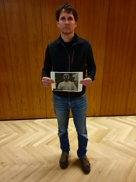Jan Schalauske steht vor einer sehr dunklen Wand und hält ein Foto hoch.