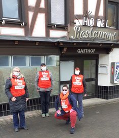 Eine Gruppe Menschen in roten Warnwesten mit dem Schriftzug "Hier ist Die LINKE" steht vor einem Fachwerkhaus