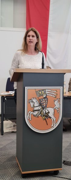 Eine blonde Frau steht an einem Redner*innenpult mit dem Logo der Stadt Marburg