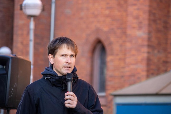 Ein Mann mit Mikrofon steht vor einem Backsteingebäude.
