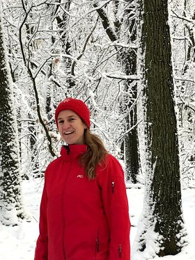 Tanja Bauder-Woehr in roter Mütze und roter Jacke lachend im verschneiten Wald.